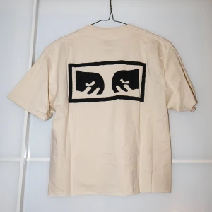 Beige t-shirt från Obey - Säljer en beige t-shirt från Obey i storlek S. Den är gjord av 100% bomull och har ett svart tryck på både fram- och baksidan. Perfekt för en avslappnad stil och passar till alla säsonger. T-shirten är i mycket bra skick och redo för nya äventyr! 