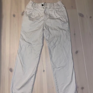Vita byxor från Jack & Jones - Säljer ett par vita byxor från Jack & Jones i bra skick. De har en elastisk midja och en knapp framtill. Perfekta för en avslappnad stil och passar till både vardag och fest. Byxorna är bekväma och lätta att matcha med olika toppar.