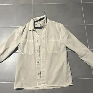 Säljer en snygg beige overshirt från Zara i mycket bra skick. Den har långa ärmar och knappar framtill, perfekt för lager-på-lager-stilen. Materialet känns som en blandning av bomull och jeans, vilket gör den både bekväm och hållbar. Två praktiska bröstfickor för extra stil och funktion. Passar perfekt till höst och vår!