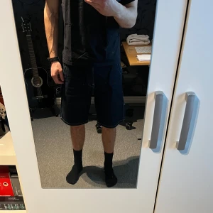 Svarta jeansshorts - Säljer ett par mörkblå jeansshorts i nytt skick. De har en loose passform och är perfekta för sommaren. Perfekta för en avslappnad stil! Byxorna är använda typ två gånger, säljer dem för att de inte kom till användning