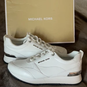 HELT NYA Vita sneakers från Michael Kors - Säljer ett par snygga oanvända vita sneakers från Michael Kors i nytt skick. Skorna har en stilren design med silverdetaljer och snörning. Perfekta för både vardag och festliga tillfällen. 