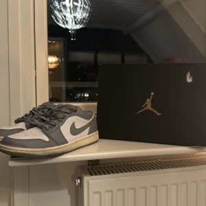Nike Air Jordan 1 Low i grått och vitt ”STORLEK 38 - Säljer ett par Nike Air Jordan 1 Low i grått och vitt. Skorna är i mycket bra skick och har en snygg design med klassisk snörning. Perfekta för både vardag och fest. Kommer med originalkartong. Passa på att köpa dessa stilrena sneakers!
