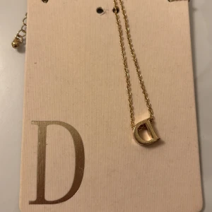 Guldhalsband med bokstaven D - Snyggt guldhalsband från Primark med en hängande bokstav D. Perfekt för att ge en personlig touch till din outfit. Halsbandet är gjort av minst 50% återvunnet metallmaterial. Enkelt och stilrent för vardag eller fest!och har aldrig använt 💘