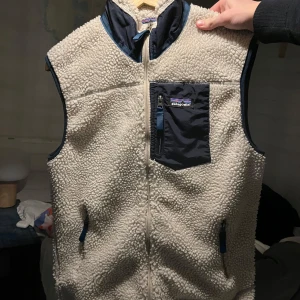 Patagonia fleeceväst - Säljer en supermysig vit fleeceväst från Patagonia. Skitbra skick 9,5/10! Den har en dragkedja fram och en praktisk bröstficka med dragkedja. Perfekt för kyliga dagar när du vill hålla dig varm och bekväm. Passar både för vardag och utomhusaktiviteter. L Passar exakt som M.