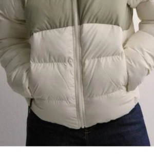 Beige och grön dunjacka från The North Face - Helt ny! Köpte fel storlek. Säljer en supermysig dunjacka från The North Face i beige och grön. Perfekt för kalla dagar med sin pufferstil och dragkedja framtill. Jackan har långa ärmar och är i mycket bra skick. Den är både snygg och praktisk för vintern!