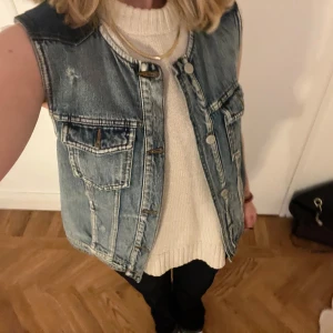 Jeansväst  - Säljer en snygg jeansväst i blått med knappar framtill. Västen har en klassisk design med två bröstfickor och är perfekt för lager-på-lager-stil. Passar bra till både vardag och festliga tillfällen. 