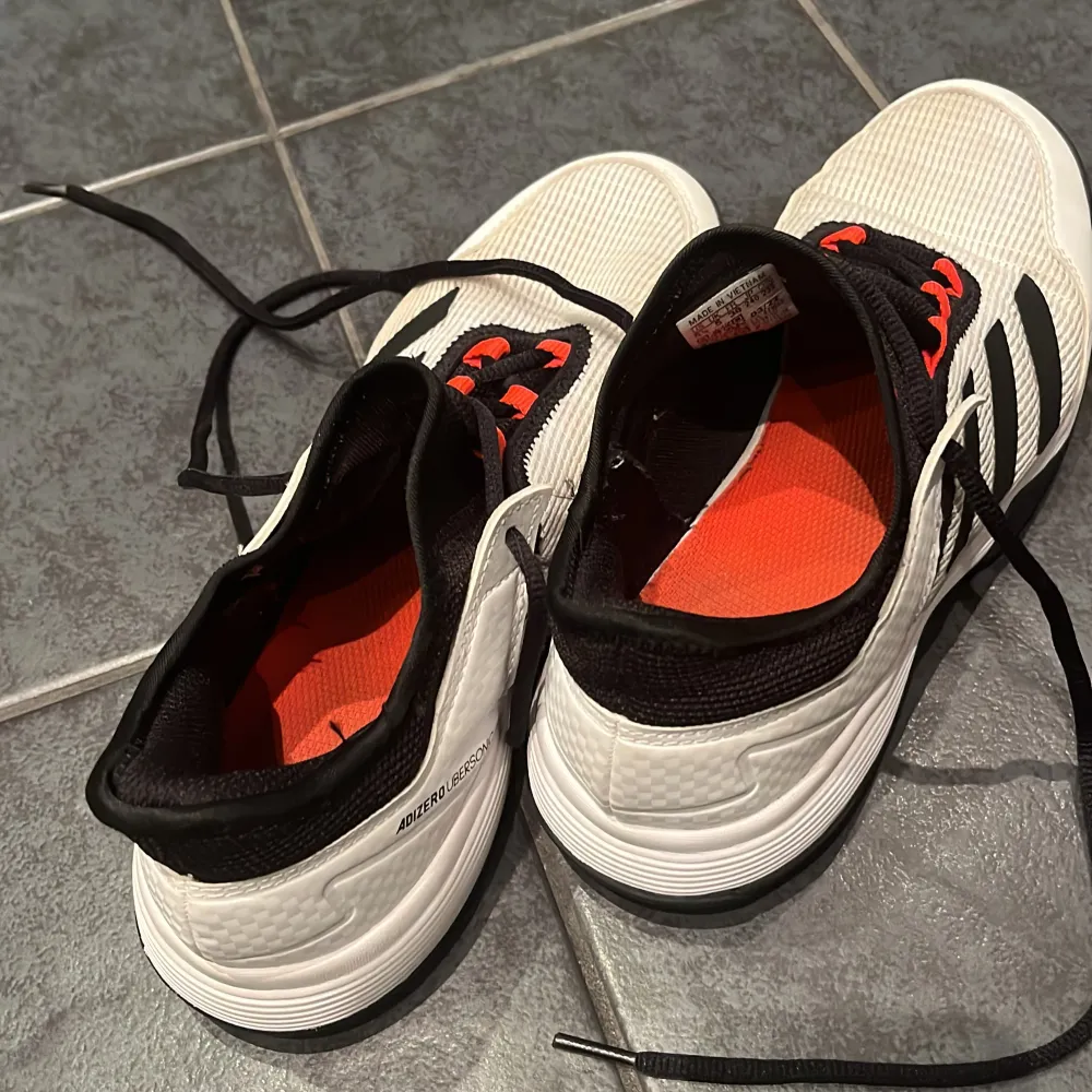 Säljer ett par Adidas sneakers i svart och vitt med coola röda detaljer. Skorna har snörning och är i mycket bra skick, lite gulnat i tyget och någon fläck som kan gå att tvätta bort. Storlek 38.. Skor.