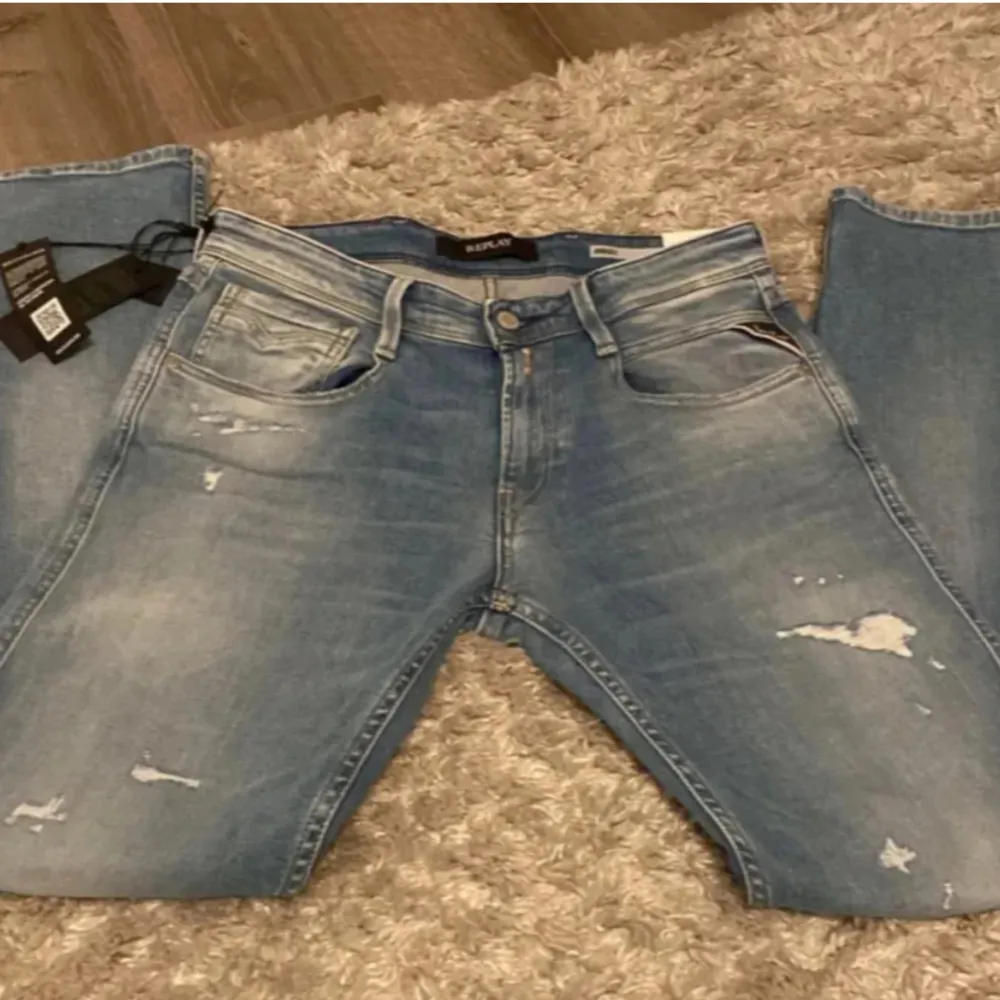 Säljer ett par snygga ljusblå jeans från Replay i nytt skick. De har en modern, distressed look med slitningar på framsidan. Perfekta för en casual stil och passar till både vardag och fest. Midjan är normal och de har en klassisk femficksdesign.. Jeans & Byxor.