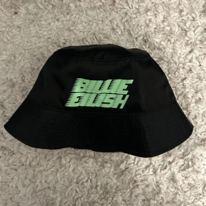 Svart bucket hat med grön text - Snygg svart bucket hat med cool grön text på framsidan. Perfekt för att ge din outfit en trendig touch. Passar bra till både vardag och festivaler. Materialet känns lätt och bekvämt.