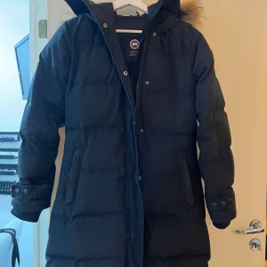 Canada goose jacka  - Säljer en svart dunjacka från Canada Goose i mycket bra skick. Jackan har en lång modell med pälsdetalj på huvan och praktiska fickor. Perfekt för kalla vinterdagar! 🖤! En utav fickorna så har dragkedjan gått sönder lätt o fixa men där av priset! Pris går o diskutera vid snabb affär 