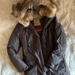 Brun parkajacka med pälsdetaljer - Säljer en snygg brun parkajacka från Parajumpers i mycket bra skick. Jackan har en stor, fluffig pälsfodrad huva och flera praktiska fickor. Perfekt för kalla vinterdagar! 
