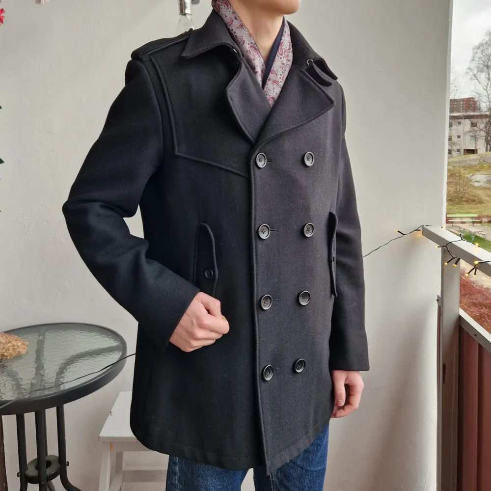 Snygg svart skepparkavaj i ullblandning med dubbelknäppning och axelklaffar. Perfekt för höst och vinter. Modellen är 180cm lång och rocken är från HM. Skick 8/10. Takit.