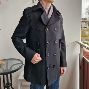 Svart rock i ullblandning - Snygg svart skepparkavaj i ullblandning med dubbelknäppning och axelklaffar. Perfekt för höst och vinter. Modellen är 180cm lång och rocken är från HM. Skick 8/10