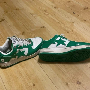 Gröna och vita sneakers från Bape - Säljer ett par snygga gröna och vita sneakers från Bape i bra skick. De har en cool stjärndetalj på sidan och klassisk snörning. Perfekta för att ge din outfit en färgklick! Sulan är grön och matchar ovandelen perfekt. Ska såklart rengöras 