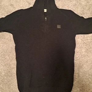 Svart stickad tröja från !Solid - Säljer en snygg svart stickad tröja från !Solid. Den har en dragkedja framtill och en liten logotyp på bröstet. Perfekt för kyliga dagar och passar till både vardag och fest. Tröjan är i mycket bra skick och redo för en ny ägare!