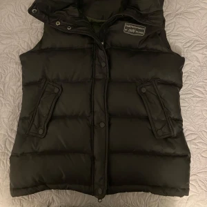Svart dunväst från Peak Performance - Säljer en svart dunväst från Peak Performance i storlek M. Västen har en stilren design med knappar och dragkedja framtill. Perfekt för höst och vinter, håller dig varm och bekväm. Den är i  bra skick och redo för nya äventyr!