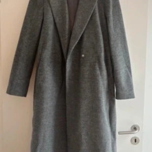 Grå fodrad kappa med bälte fiskbensmönstrad - Säljer en stilren grå kappa i fiskbensmönster. Kappan är fodrad och i ett mycket bra skick. Den har en klassisk design  med långa ärmar och ett bälte i midjan för en snygg passform. Perfekt för höst och vinter! 🧥