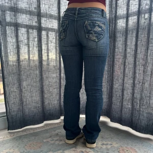 Mörkblå jeans med broderade bakfickor - Ett par snygga mörkblå jeans med unika broderade detaljer på bakfickorna. Midjemått 35 cm Grenmått 19 cm innerbenslängd 81 cm