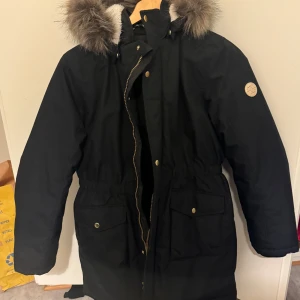 Svart parkajacka med pälsdetaljer - Säljer en svart parkajacka i mycket bra skick. Jackan har en mysig pälsfodrad huva och praktiska fickor framtill. Perfekt för kalla vinterdagar! 🖤