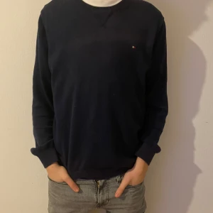 Mörkblå tröja från Tommy Hilfiger - Säljer denna Tommy Hilfiger hoodien till ett väldigt billigt pris. Den är i ett 6/10 skick därav det billiga priset, det finns en slitning precis över märket som går att tvätta bort hos en kemtvätt. Tveka inte att ställa några frågor om du har några! 