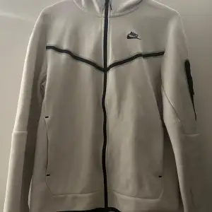 Säljer en snygg vit hoodie från Nike i storlek S. Den har en dragkedja framtill och en cool svart detalj som går över bröstet. Perfekt för både träning och vardag. Hoodien är i mycket bra skick och superbekväm att ha på sig. Passar perfekt till höst och vår!