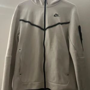 Vit hoodie från Nike - Säljer en snygg vit hoodie från Nike i storlek S. Den har en dragkedja framtill och en cool svart detalj som går över bröstet. Perfekt för både träning och vardag. Hoodien är i mycket bra skick och superbekväm att ha på sig. Lite fläckar på baksidan men kommer nog försvinna i tvättmaskinen.Passar perfekt till höst och vår! 