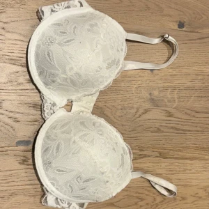 Vit spets-bh - Säljer en elegant vit bh med spetsdetaljer. Den har justerbara axelband och en klassisk hakknäppning bak. Perfekt för att känna sig både bekväm och stilren. Passar till både vardag och fest! Storlek 75 c🩷