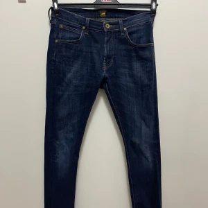 Mörkblå jeans från Lee - Säljer ett par snygga mörkblå jeans från Lee i bra skick. De har en klassisk femficksdesign med guldfärgade knappar och nitar. Jeansen är slim fit. Pris kan diskuteras.