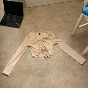 Beige långärmad topp från SHEIN - Säljer en snygg beige långärmad topp från SHEIN i storlek M. Toppen är croppad med en trendig snörning framtill som ger en cool look. Perfekt för både vardag och fest! 💫