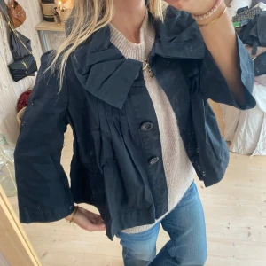 Svart kappa med rosett - Säljer en superfin svart kappa med stora knappar och en snygg rosett vid kragen. Den har en loose passform och trekvartsärmar, perfekt för höst och vår. Jackan är i bra skick och passar både till vardags och fest. Ett måste i garderoben! 🖤