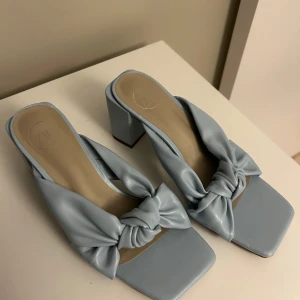 Ljusa blå klackskor med knyt - Säljer ett par ljusblå klackskor med en snygg knytning framtill. De har en fyrkantig tå och en stabil klack som gör dem bekväma att gå i. Perfekta för både vardag och fest!