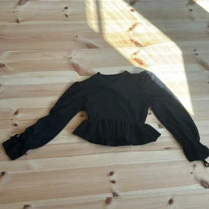 Svart topp från SHEIN - Säljer en snygg svart topp från SHEIN. Den har långa ärmar och en croppad design med volangdetaljer i nederkanten. Perfekt för en kväll ute eller en festlig tillställning. Toppen är i bra skick och redo för nya äventyr!