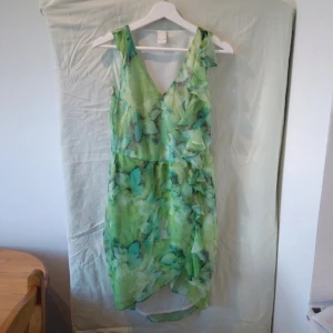 Grön blommig klänning från Vila - Säljer en superfin grön klänning från Vila med ett härligt blommigt mönster. Klänningen är ärmlös och har en v-ringad design som ger en somrig känsla. Perfekt för en fest eller en dag ute i solen!