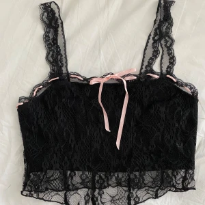 Svart spetslinne med rosa rosett - Kort svart spetslinne med rosa rosett. Skulle gissa att det är storlek xs. Syntetiskt material. Vet ej märket. Köpt second hand 