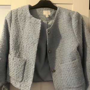 Ljusblå jacka från H&M - Säljer en superfin ljusblå jacka från H&M, aldrig använd så i princip nyskick. Den har en snygg, texturerad yta och knäpps med stiliga knappar framtill. Jackan har långa ärmar och två praktiska fickor. Perfekt för vår och höst! ord pris : 453kr och jag säljer för 300 kr <3