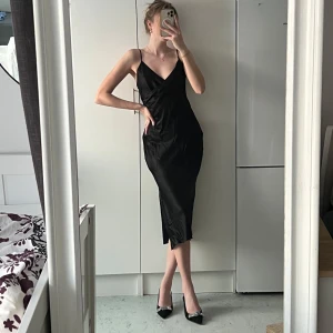 Svart midiklänning - Simepl svart midiklänning med justerbala axelband, omlott design och slits. Perfekt för en stilren look. Klänningen är figursydd, väldigt nätt och flowy, ger en fin siluett. Köpt på Zara och endast använd vid ett tillfälle