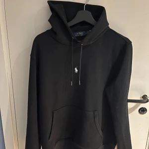 Svart hoodie från Ralph Lauren - Säljer en stilren svart hoodie från Ralph Lauren med det klassiska logotypbroderiet på bröstet. Hoodien har en justerbar dragsko i huvan och en praktisk magficka. Perfekt för en avslappnad look. pris kan förhandlas vid snabb affär