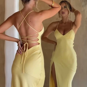 Ljusgul balklänning  - Elegant gul långklänning med smala axelband och djup slits. Klänningen har en vacker öppen rygg med korsad snörning som ger en unik look. Perfekt för balen 