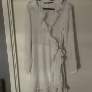 Studentklänning | Vit omlottklänning med volang - Elegant vit omlottklänning med volangdetaljer och knytning i midjan. Klänningen har långa ärmar och en feminin design som passar perfekt för speciella tillfällen. Perfekt till sommar, skolavslutning och studenten☺️❤️🥰💖