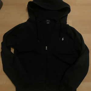 Mörkblå hoodie från Polo Ralph Lauren - Säljer en stilren mörkblå hoodie från Polo Ralph Lauren med dragkedja och det klassiska logotypbroderiet på bröstet. Perfekt för en avslappnad look. Hoodien har långa ärmar och en bekväm huva. Ser mörk ut på bilden men är mörkblå kan skicka en extra bild där den är tydlig skriv vid minsta intresse!