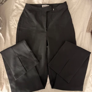 Svarta kostymbyxor från NA-KD - Snygga svarta kostymbyxor från NA-KD med hög midja och dragkedja framtill. Byxorna har en stilren design med raka ben och diskreta bakfickor. Även en snygg slits nedtil. Perfekta för en elegant look.