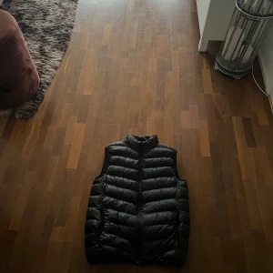 Svart dunväst från Brave Soul - Säljer en stilren svart dunväst från Brave Soul. Västen har en quiltad design och är perfekt för kyligare dagar. Den är lätt och smidig att bära, vilket gör den till ett mångsidigt plagg i garderoben. NY PRIS 400kr 