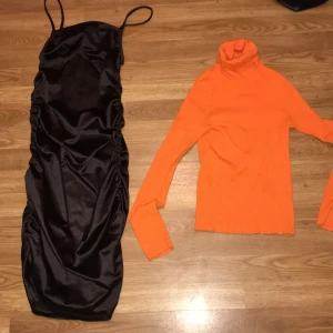 Svart satin klänning med smala axelband - Elegant svart klänning i satin med smala axelband och rynkade detaljer längs sidorna. Perfekt för en stilren look.