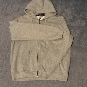 Grå zip up från polo Ralph lauren - Säljer en stilren grå zip up från polo Ralph Lauren, den är i L (custom fit) och säljes då den är för liten runt mina axlar. Den är helt ny, fick i present. Priset är inte hugget i sten!