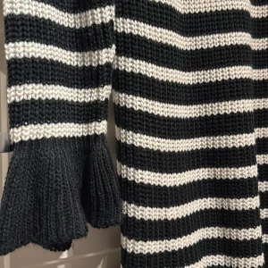 Randig stickad klänning - Snygg randig stickad klänning med volangdetaljer vid ärmslut och nederkant. Klänningen har en kombination av svart och vit färg med en mysig passform. Perfekt för kyligare dagar.