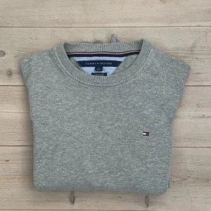 Grå tröja från Tommy Hilfiger - Säljer en stilren grå tröja från Tommy Hilfiger i mjuk bomull. Tröjan har en liten broderad logotyp på bröstet och ribbade muddar vid ärmslut och nederkant. Perfekt för en avslappnad look. Den är köpt i USA och i perfekt skick inga defekter🤩