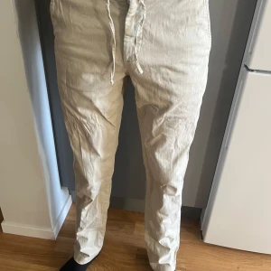 Beige linnebyxor med snörning - Snygga beige linnebyxor med avslappnad passform och snörning i midjan. Byxorna har två sidofickor.