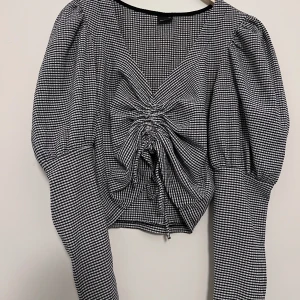 Svartvit rutig blus från Gina Tricot - Säljer en snygg svartvit rutig blus från Gina Tricot i storlek XS. Blusen har långa ärmar och en knytning framtill som ger en fin detalj. Perfekt för att ge din outfit en trendig touch.