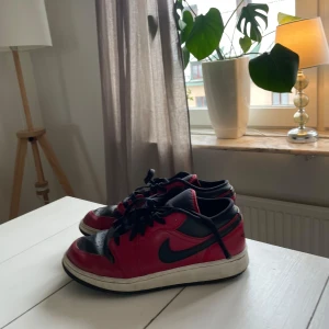 Nike Air Jordans i rött och svart - Snygga Nike Air Jordans i en klassisk röd och svart färgkombination. Skorna har en ikonisk design med snörning och den välkända Nike-loggan på sidan. Perfekta för dig som vill ha en stilren och sportig look.