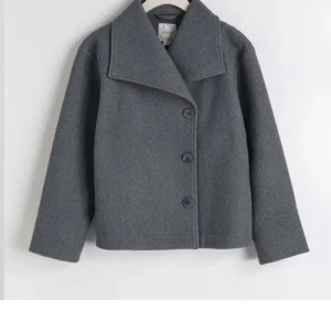 Grå kappa med knappar - Snygg grå kappa med stora knappar och bred krage. Perfekt för kyligare dagar med sin stilrena design och långa ärmar. En klassisk look som funkar till det mesta.